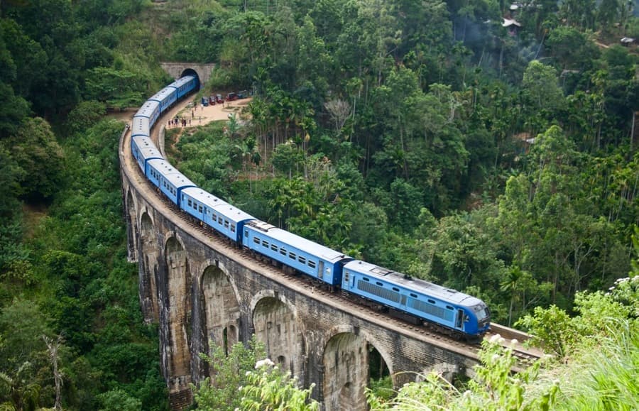 A blue train crossing the Nine Arch Bridge through the hills